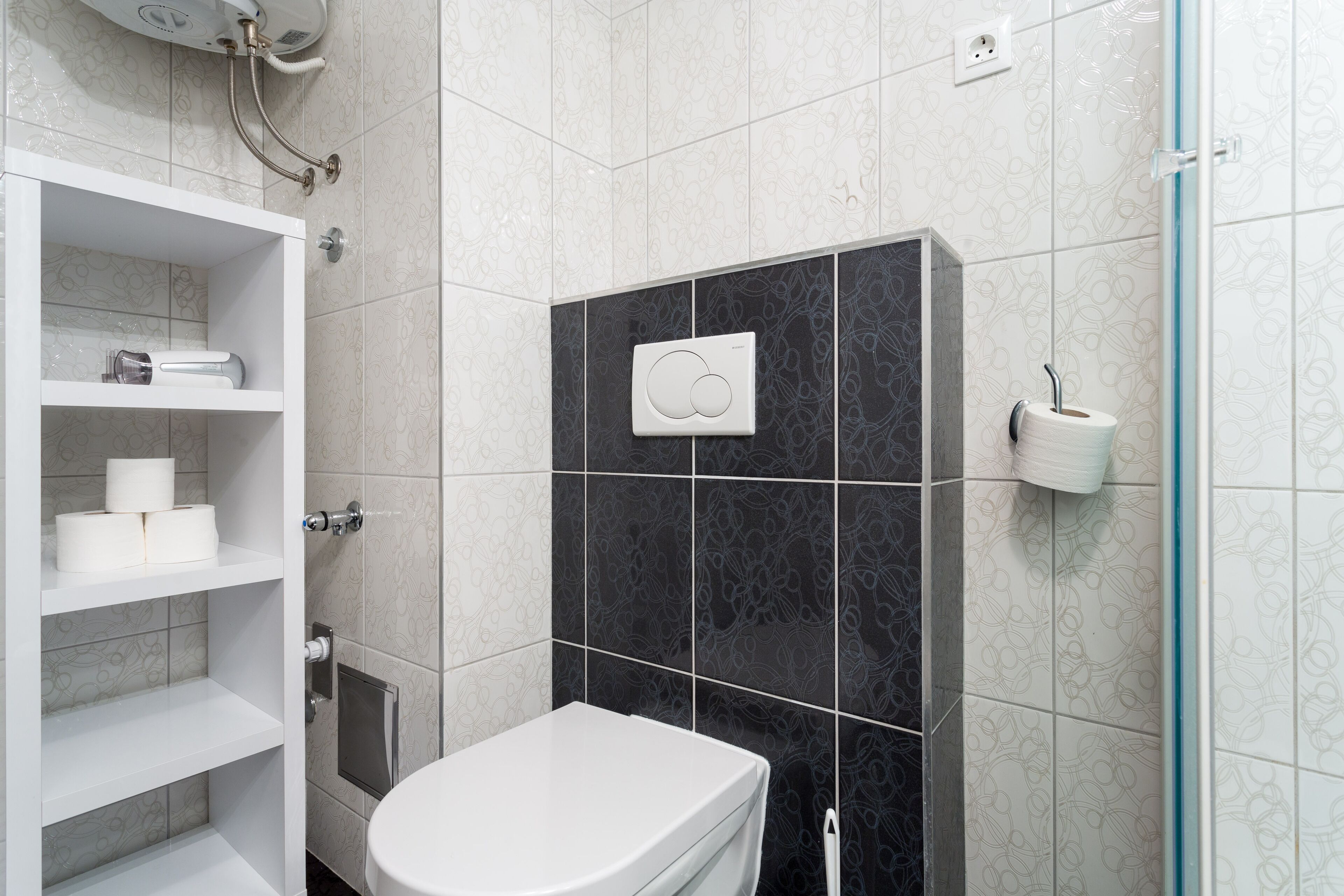 Un baño moderno con inodoro, repisas con artículos de aseo, dispensador de toallas y zona de ducha.