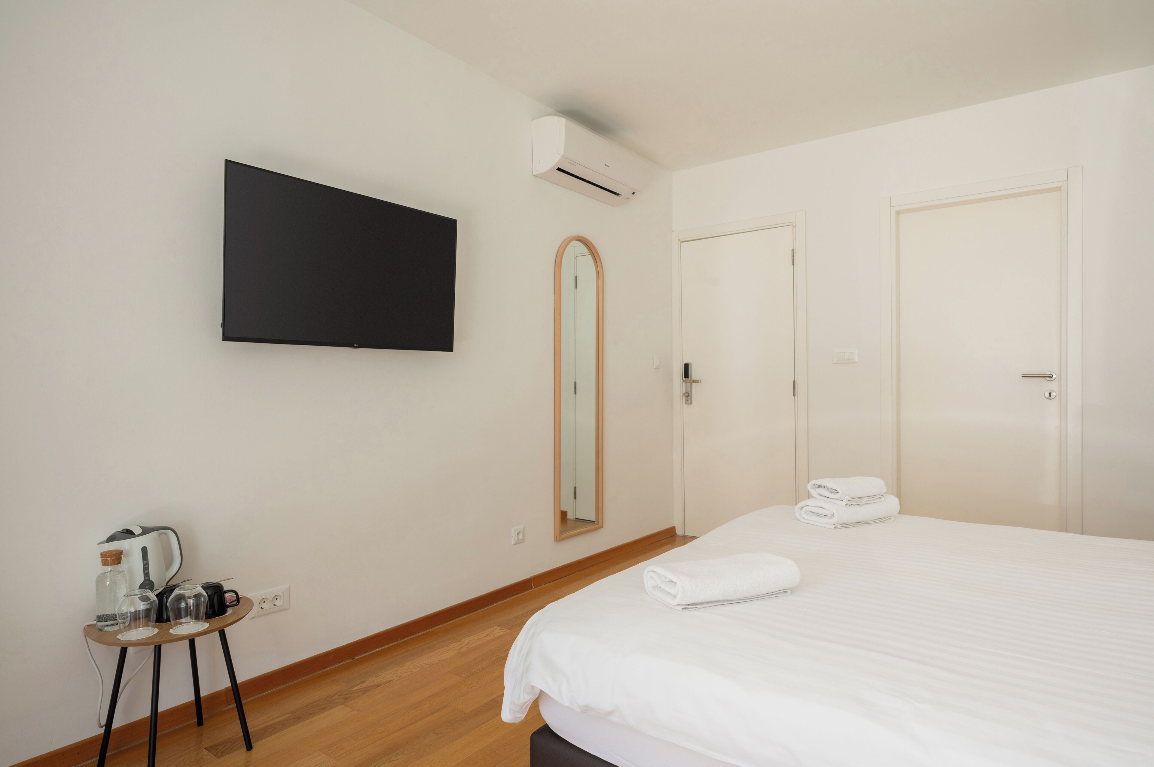 Una habitación de hotel con cama, televisor de pantalla plana, una mesita con tetera y tazas, un espejo y dos puertas.
