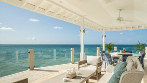 A covered outdoor seating area with a view of the ocean, featuring a table, chairs, and a sofa. - Blue Waters Resort - Rock Cottage (Antigua and Barbuda)