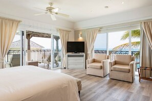 Een ruime slaapkamer met een groot bed, twee fauteuils, een televisie en een balkon met uitzicht op de oceaan.