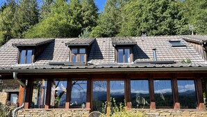 Un edificio de piedra con techo inclinado, varias ventanas y vistas al bosque circundante.