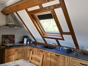A kitchen with wooden cabinets, a skylight, a stainless steel range hood, and a window overlooking greenery.