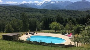 Una piscina con sillas de descanso, una estructura de madera y montañas al fondo.