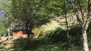 Una cabaña rústica con techo de paja, rodeada de árboles y un área cubierta de césped.