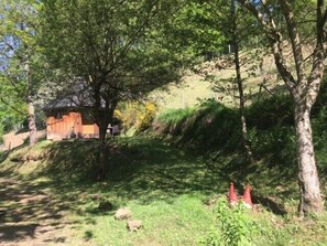 A rustic cabin with a thatched roof, surrounded by trees and a grassy area.