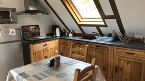 A kitchen with wooden cabinets, a microwave, a refrigerator, a skylight, and a table with a placemat. - Studio-Mountain view-Wet room-Romantic (Aleu)