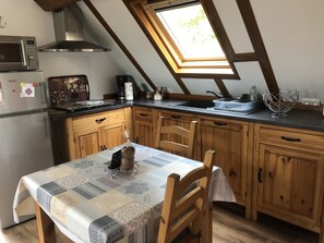 Een keuken met houten kastjes, een magnetron, een koelkast, een dakraam en een tafel met placemat.