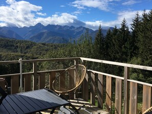 Eine Holzterrasse mit Tisch und Korbstuhl, mit Blick auf eine gebirgige Landschaft.