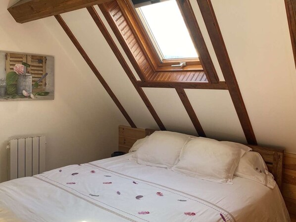 A bedroom with a sloped ceiling, a skylight, a bed with white bedding, and a radiator.