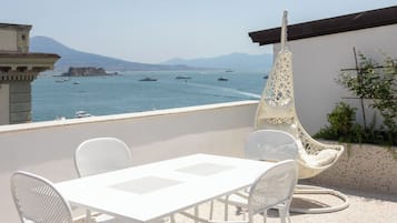 Una terrazza con tavolo e sedie bianche, una sedia a dondolo e vista sul mare con barche.
