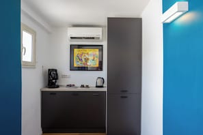 A compact kitchen with a coffee machine, a kettle, and a framed artwork on the wall.