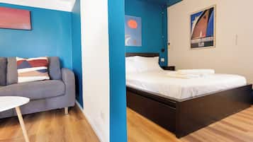 Una camera d'albergo con un letto, un divano grigio, un piccolo tavolino bianco e una parete azzurra.
