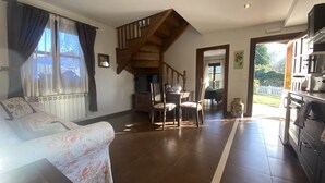 Een woonkamer met een bank, een eettafel met stoelen, een houten trap en een keuken met een fornuis.