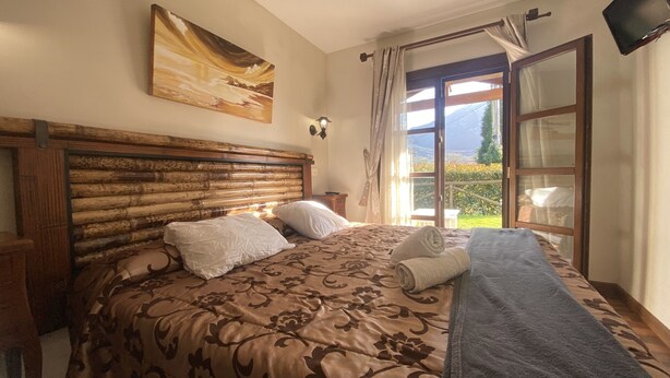 Een slaapkamer met een houten hoofdbord, een groot bed met bloemenbedrukking, een nachtkastje en een raam met gordijnen.