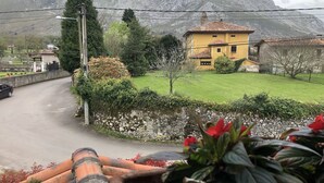 Een landweg met een geel huis, een groen gazon en bergen op de achtergrond.