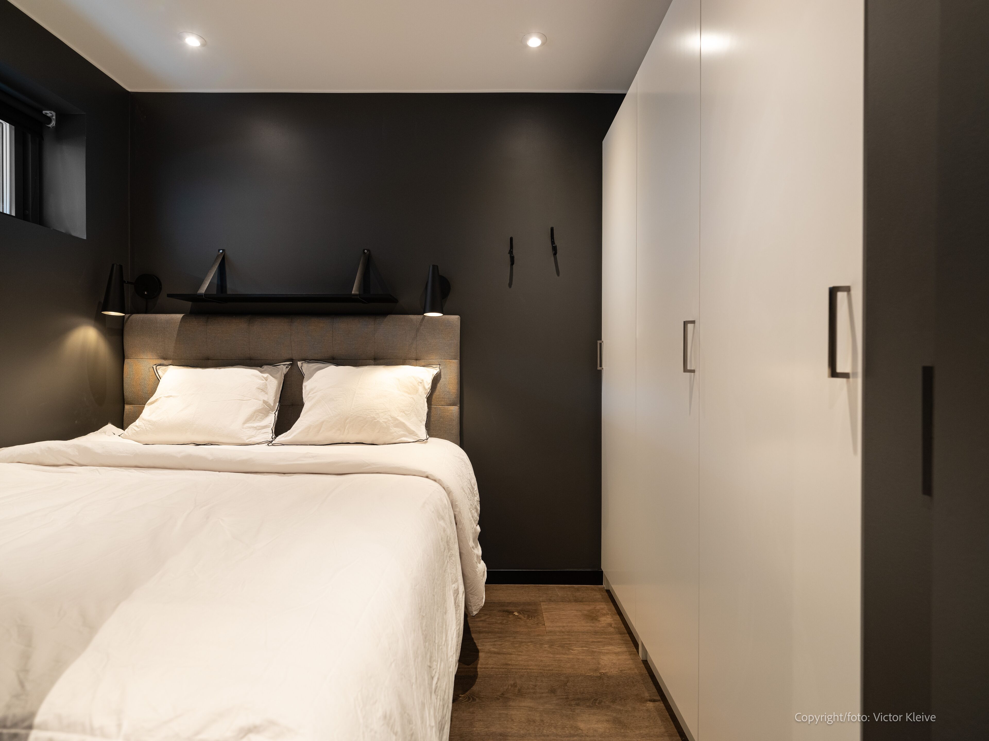 A modern bedroom with a large bed, a dark wall, and a built-in wardrobe.