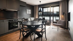 A modern kitchen with dark cabinetry, a dining table with chairs, and a large window overlooking a snowy landscape.