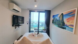 Quarto de hotel com cama, televisão de tela plana, pintura de paisagem e vista para prédios pela janela.