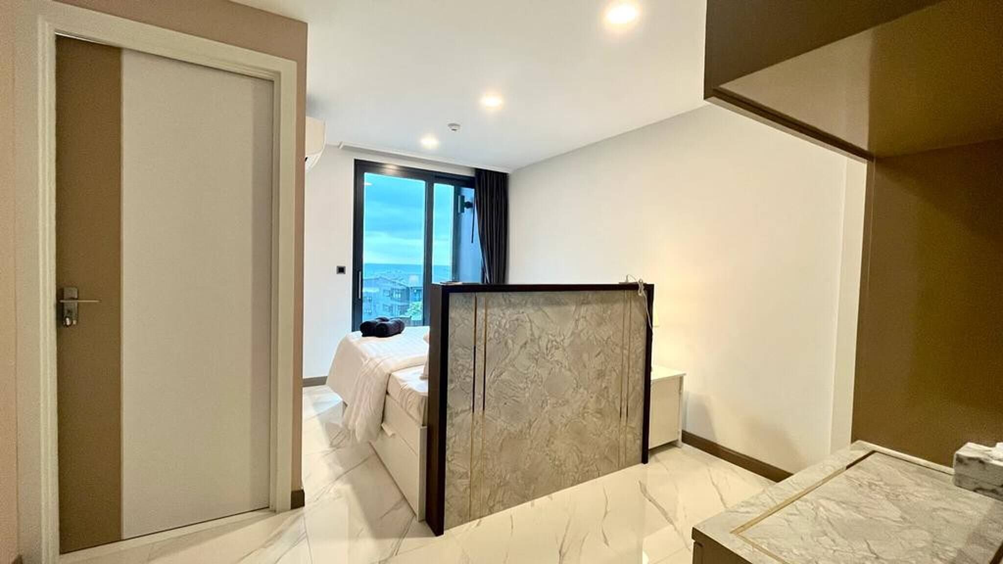 A hotel room with a bed, a view of the city, and a bathroom with a marble floor.