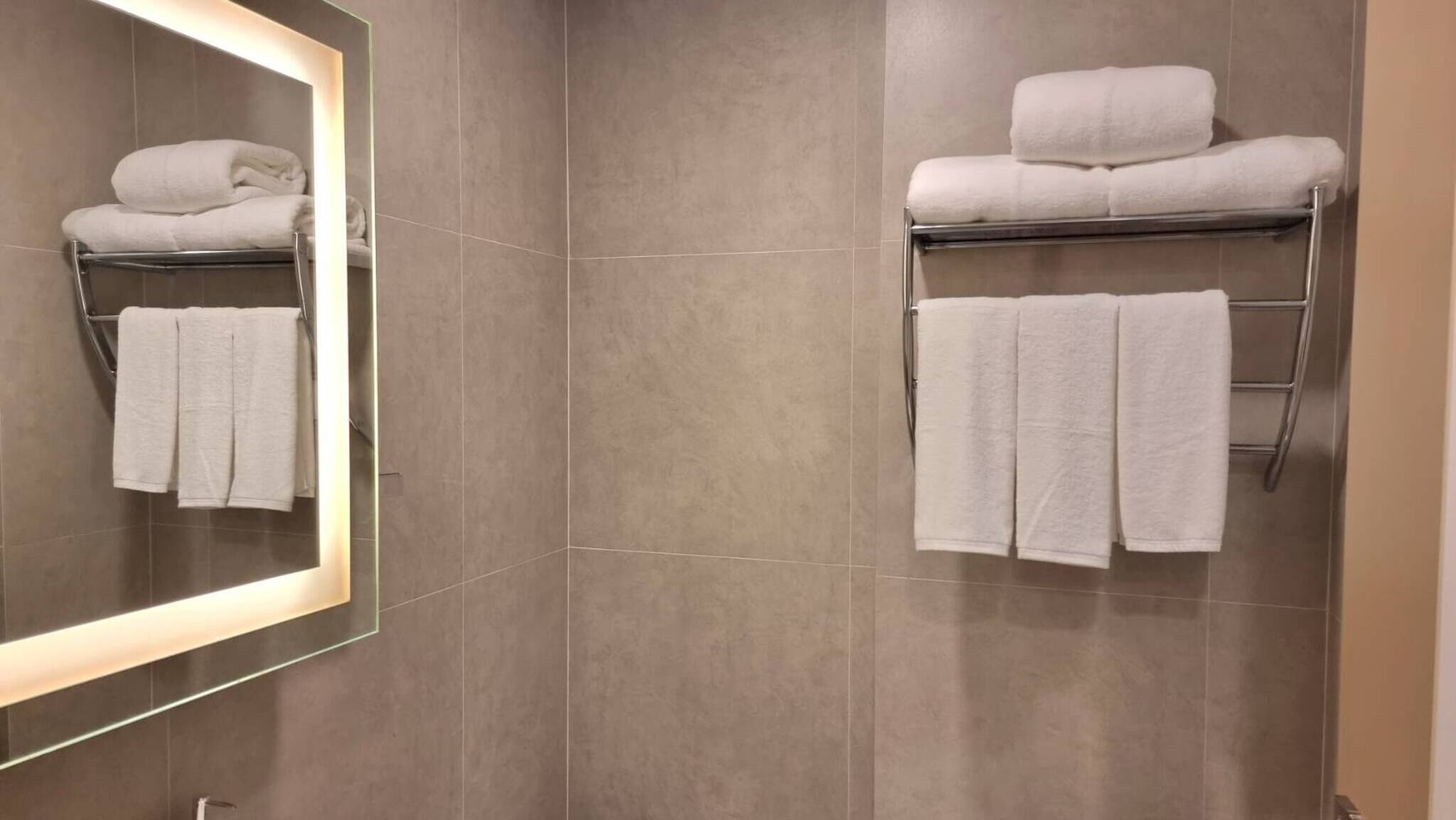 A bathroom with a large mirror, two towel racks, and grey tiles.