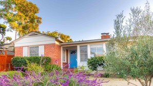 A single-story house with a blue door, surrounded by a garden with purple flowers and a tree.
