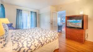A bedroom with a bed, a TV on a wooden cabinet, and a door leading to another room.
