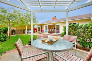 A covered patio with a round table and chairs, a brick pathway, and a house in the background.
