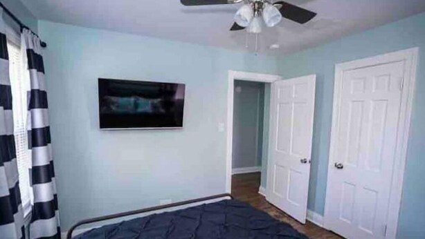 A bedroom with a bed, a ceiling fan, a TV on the wall, and a door leading to another room. - Urban Bourbon Trail Near Derby, Fair, Expo and Airport - 4 Beds, 3 BR, 2 Baths (Louisville)