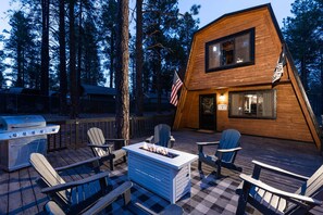 A cabin with a deck, outdoor grill, and Adirondack chairs.