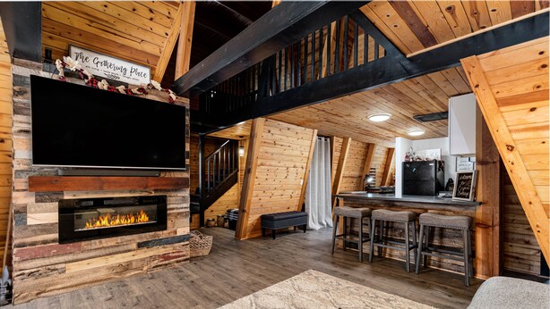 A rustic interior with a fireplace, wooden beams, a bar area, and a staircase.