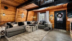 A cozy log cabin interior with a sectional sofa, a small table, and a decorative wreath on the door.