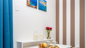A modern room with a white desk, a chair, a small shelf with a vase of flowers, and a tray with a croissant and coffee cups.