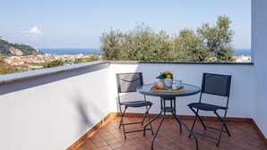 A small balcony with a round table and two chairs, a tray with a croissant, a cup, and a bowl of fruit.