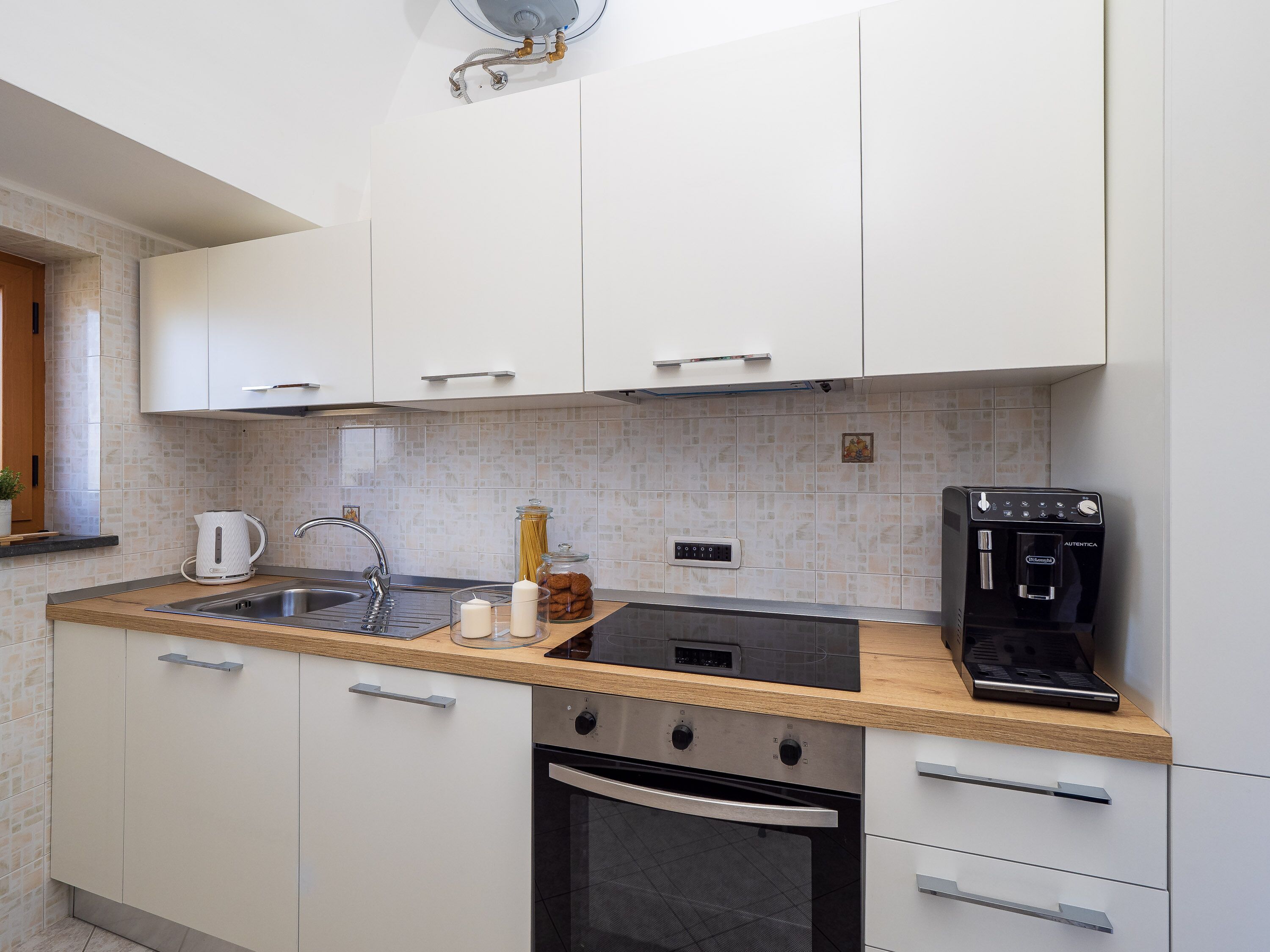 Una cocina moderna con armarios blancos, un lavamanos de acero inoxidable, una cafetera y un horno empotrado.