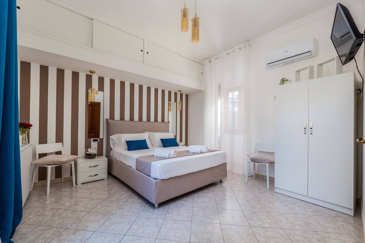A modern bedroom with a large bed, a wardrobe, a desk, and a chair.