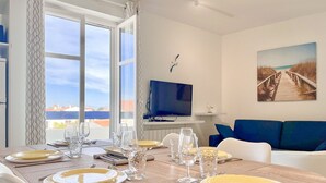 A dining area with a table set for four, a television, and a painting on the wall. - Spacious apartment with ocean view in the Chaume district (Les Sables-d´Olonne)
