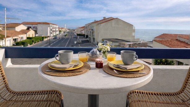 A balcony with two wicker chairs, a table set for breakfast with cups, plates, and a vase of flowers. - Spacious apartment with ocean view in the Chaume district (Les Sables-d´Olonne)