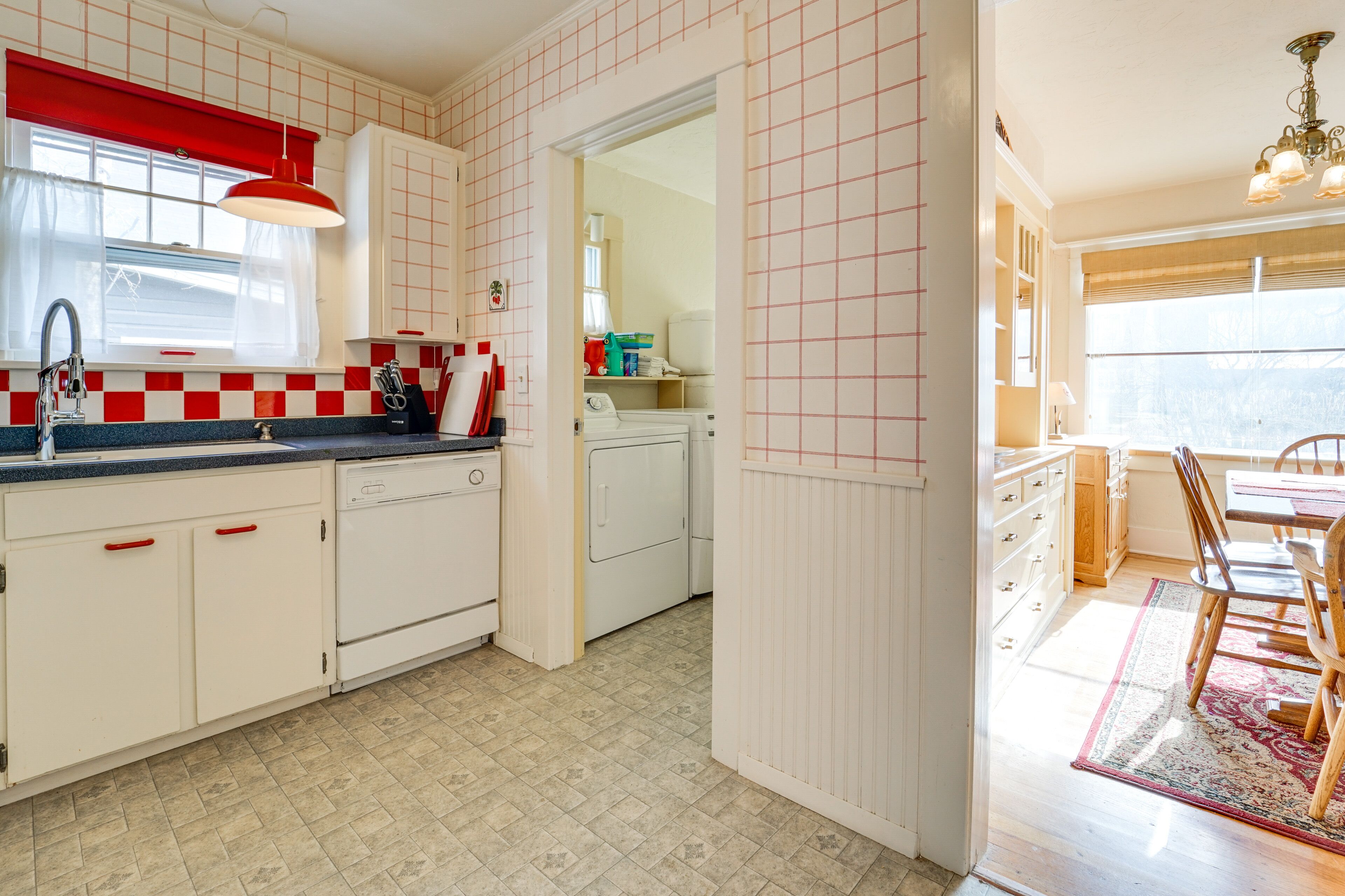 A kitchen with white cabinets, a red-framed window, and a dining area with a table and chairs.