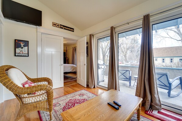 A hotel room with a wicker chair, a wooden table, a TV, and a view of the outside.