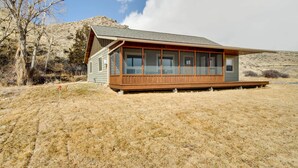 A cabin with a large windowed front section, situated in a dry, grassy area with a mountain in the background. - Beautiful Jefferson River Cabin w/ Mountain Views! (Twin Bridges)