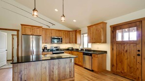 A spacious kitchen with wooden cabinets, a stainless steel refrigerator, a microwave, and a dishwasher. - Beautiful Jefferson River Cabin w/ Mountain Views! (Twin Bridges)