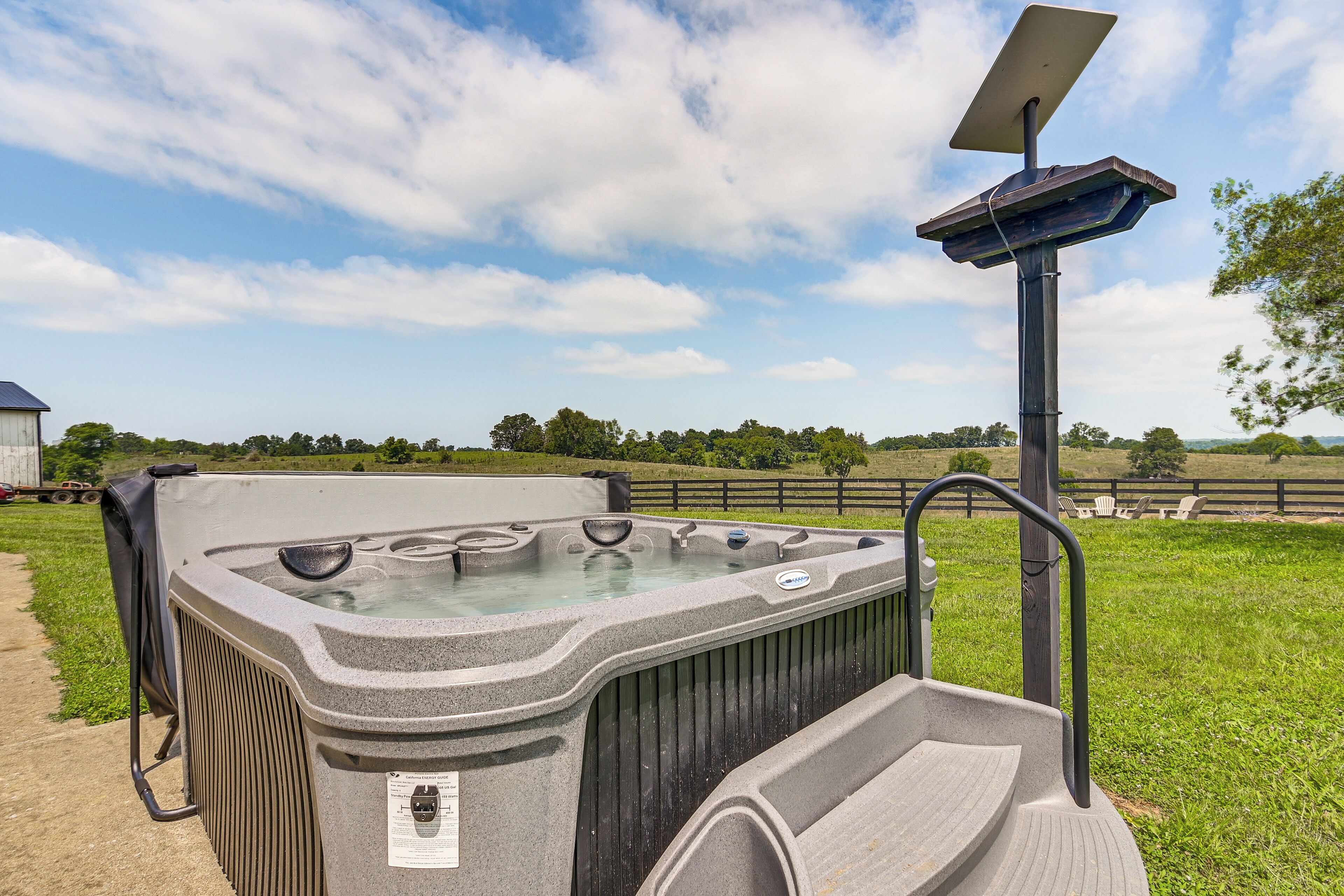 Un bain à remous équipé d’un panneau solaire, entouré d’une pelouse et d’une clôture en bois.
