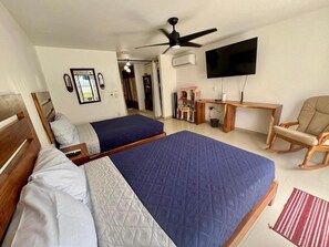 Quarto com duas camas, televisão, ventoinha no teto, escrivaninha de madeira e uma cadeira de balanço.