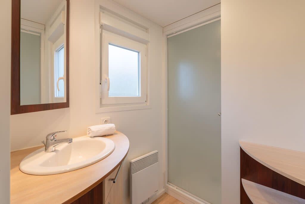 Un baño con lavabo blanco, espejo, ventana y cabina de ducha.