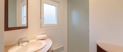 Un baño con lavabo blanco, espejo, ventana y cabina de ducha.