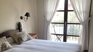 A neatly made bed with floral pillows, a wall-mounted lamp, and a window with curtains.