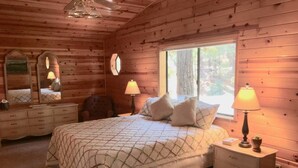 Ein Schlafzimmer mit Holzwandverkleidung, einem Bett, zwei Nachttischen mit Lampen, einer Kommode und einem großen Spiegel.
