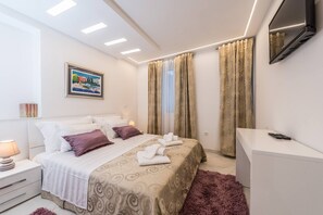 Hotellihuone, jossa on sänky, yöpöytä, televisio ja verhot.