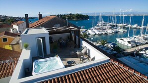 Una terraza en la azotea con jacuzzi, mobiliario exterior y vistas a un puerto deportivo con barcos.