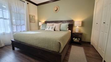 A neatly made bed with a quilt, two bedside lamps, a nightstand with a drawer, a framed picture on the wall, and a door to the right.